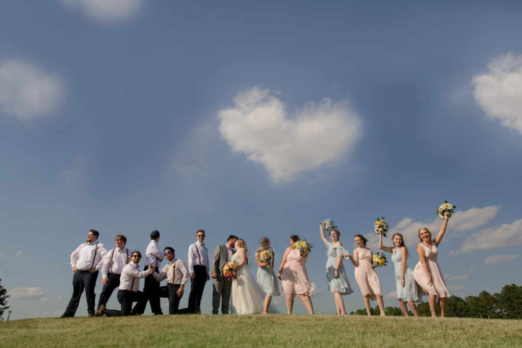 bridal party on top of hill with blue sky background and heart cloud