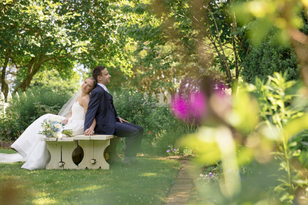 bride and groom sitting on a bench back to back in a garden