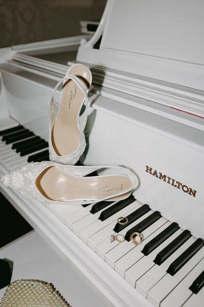 white wedding shoes and rings on a white piano