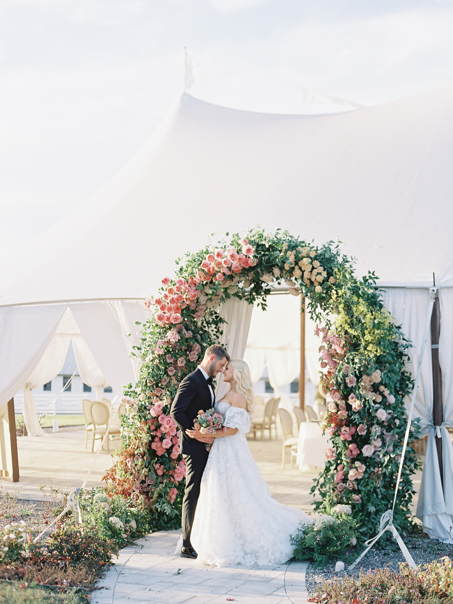 Bride and groom sharing a romantic moment under a lush floral arch at their tented Northfield Estate wedding in Charlottesville, Virginia.