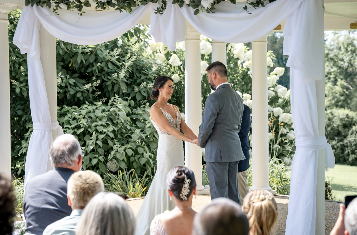 a couple stands beneath a draping white fabric in a gazebo saying their wedding vows