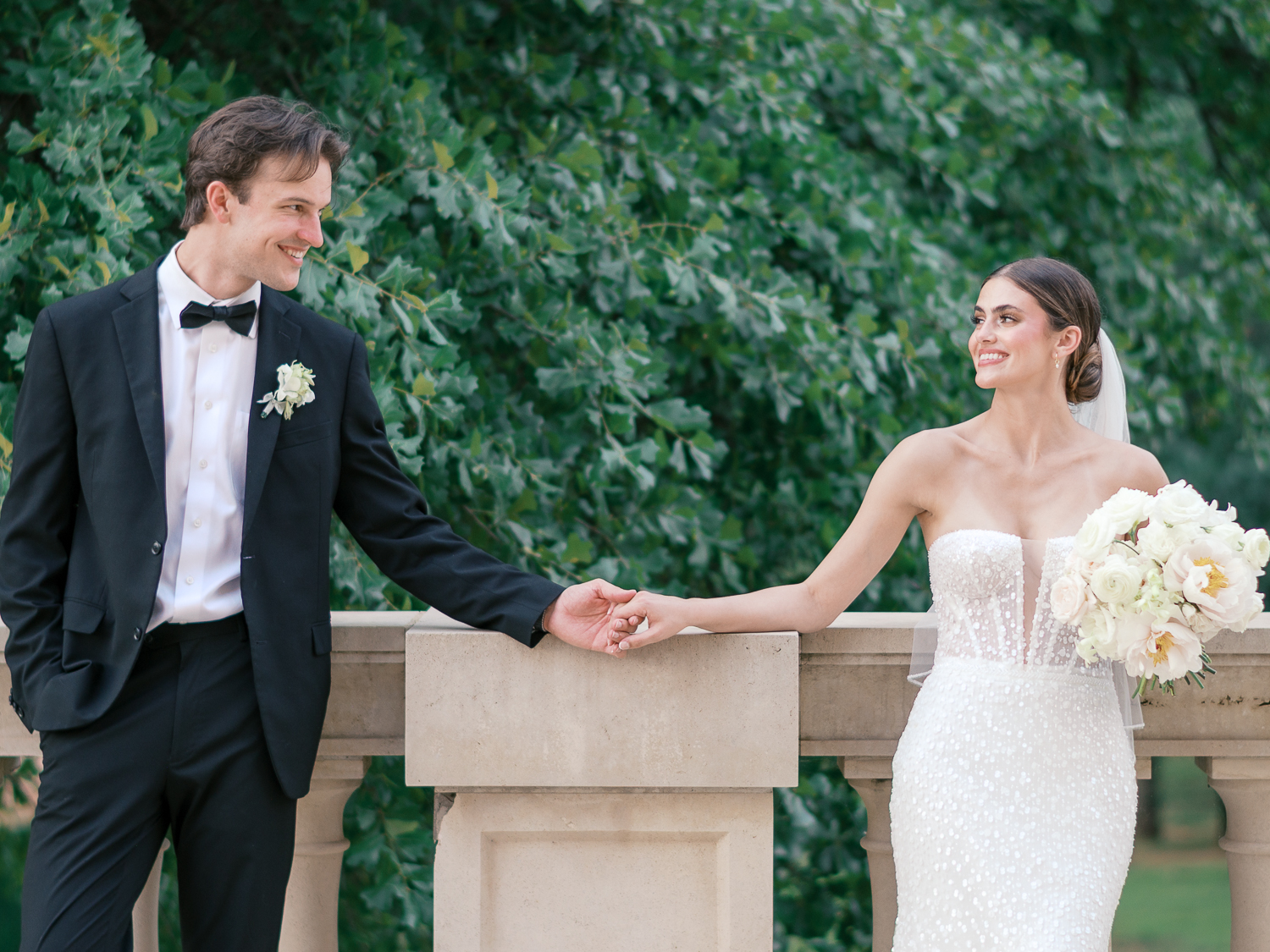 Elegant bride in a strapless beaded gown holding hands with groom in a black tuxedo for a luxury wedding portrait.